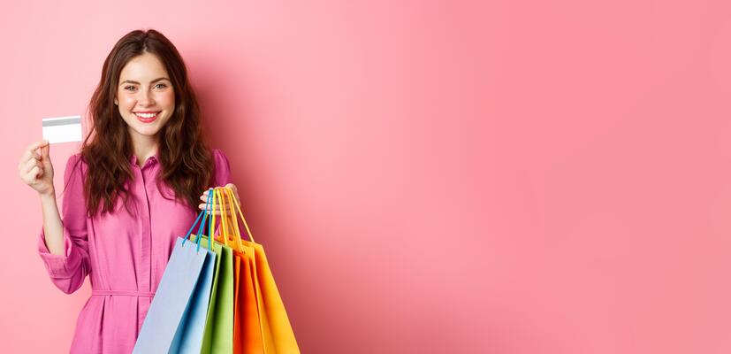 young-brunette-woman-holding-shopping-bags-showing-plastic-credit-card-and-smiling-standing-against-pink-background-photo